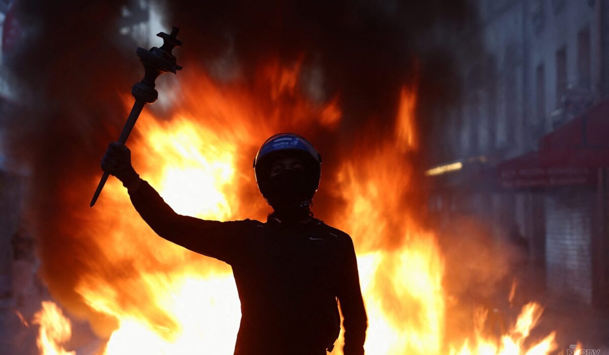 A masked protester raises an arm in front of a burning barricade during the France protests in Paris, October 2026