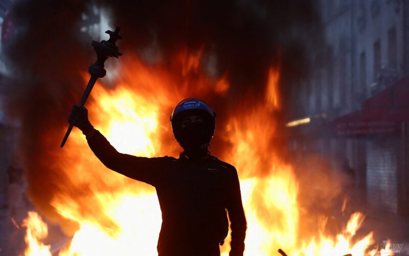 A masked protester raises an arm in front of a burning barricade during the France protests in Paris, October 2026