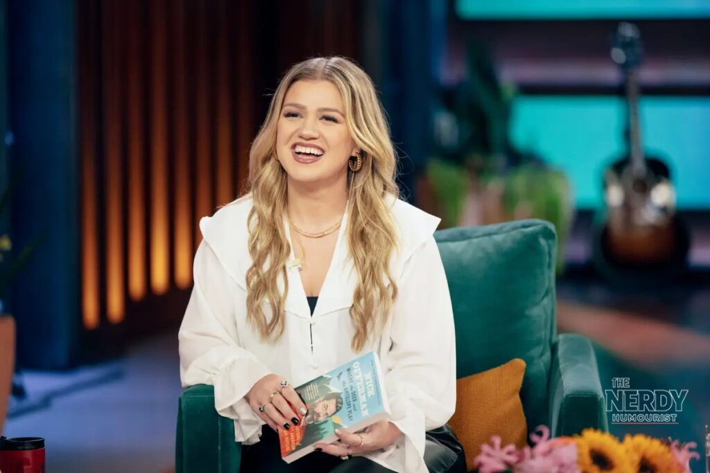 Kelly Clarkson laughing on The Kelly Clarkson Show set amid the Kelly Clarkson Art of Play feud.