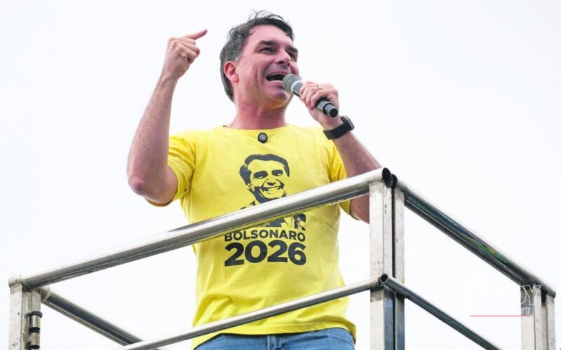 Senator Flávio Bolsonaro speaking at a 2026 campaign rally wearing a yellow "Bolsonaro 2026" shirt, after his first-place finish in the Brazil election results runoff 2026 first round