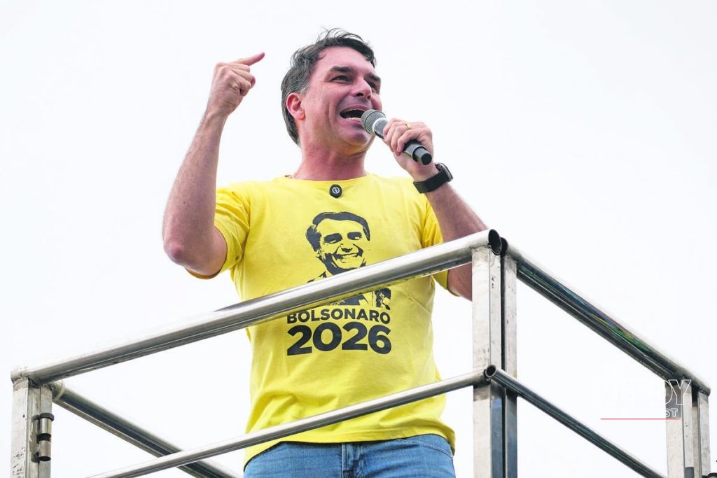 Senator Flávio Bolsonaro speaking at a 2026 campaign rally wearing a yellow "Bolsonaro 2026" shirt, after his first-place finish in the Brazil election results runoff 2026 first round