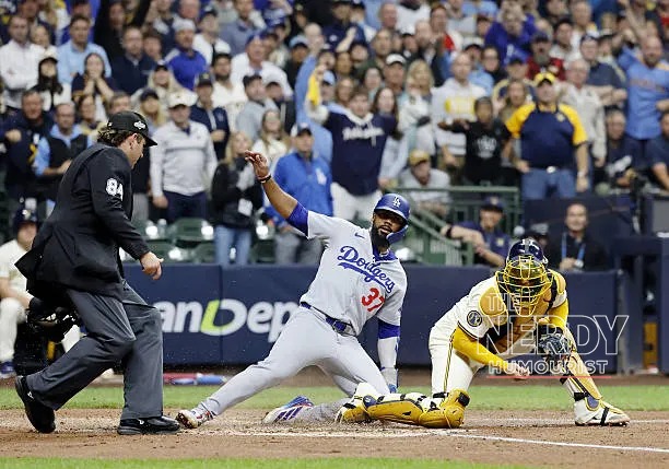 A Los Angeles Dodgers baserunner slides into home as the Milwaukee Brewers catcher applies the tag