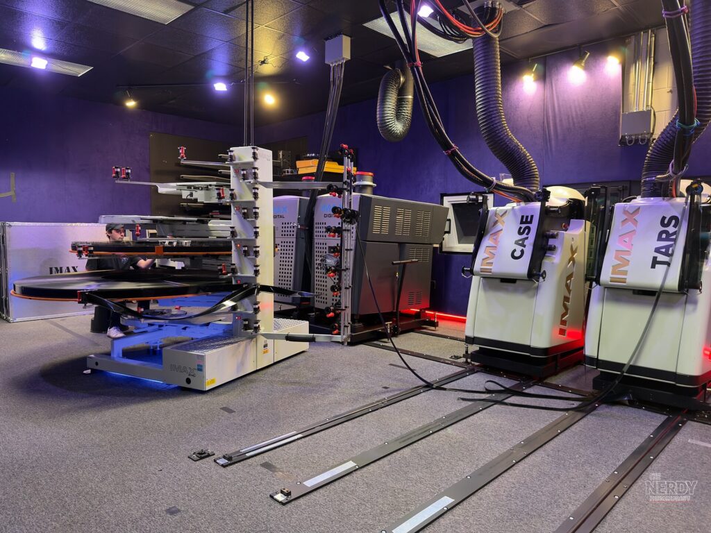 IMAX 70mm film reels running through a projector, the format powering The Odyssey IMAX re-release.