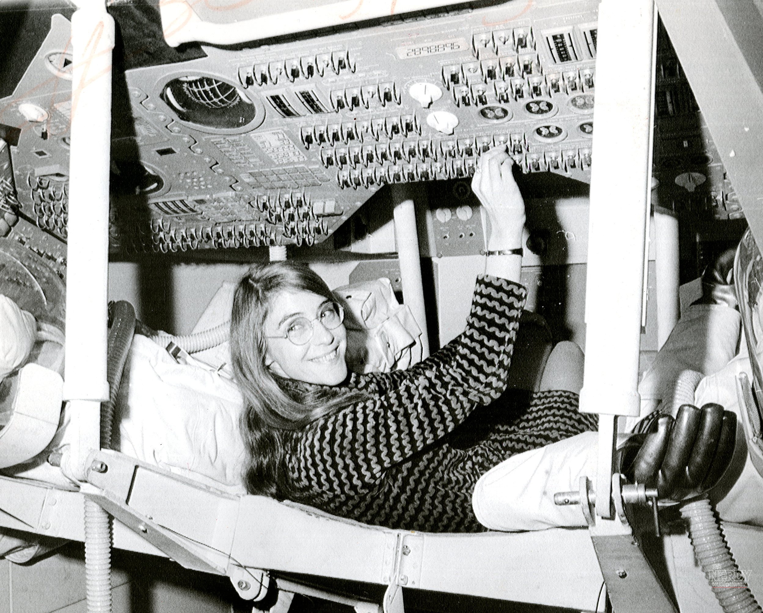 A young Margaret Hamilton sits inside an Apollo Command Module in 1969, reaching up toward the spacecraft's instrument panels.