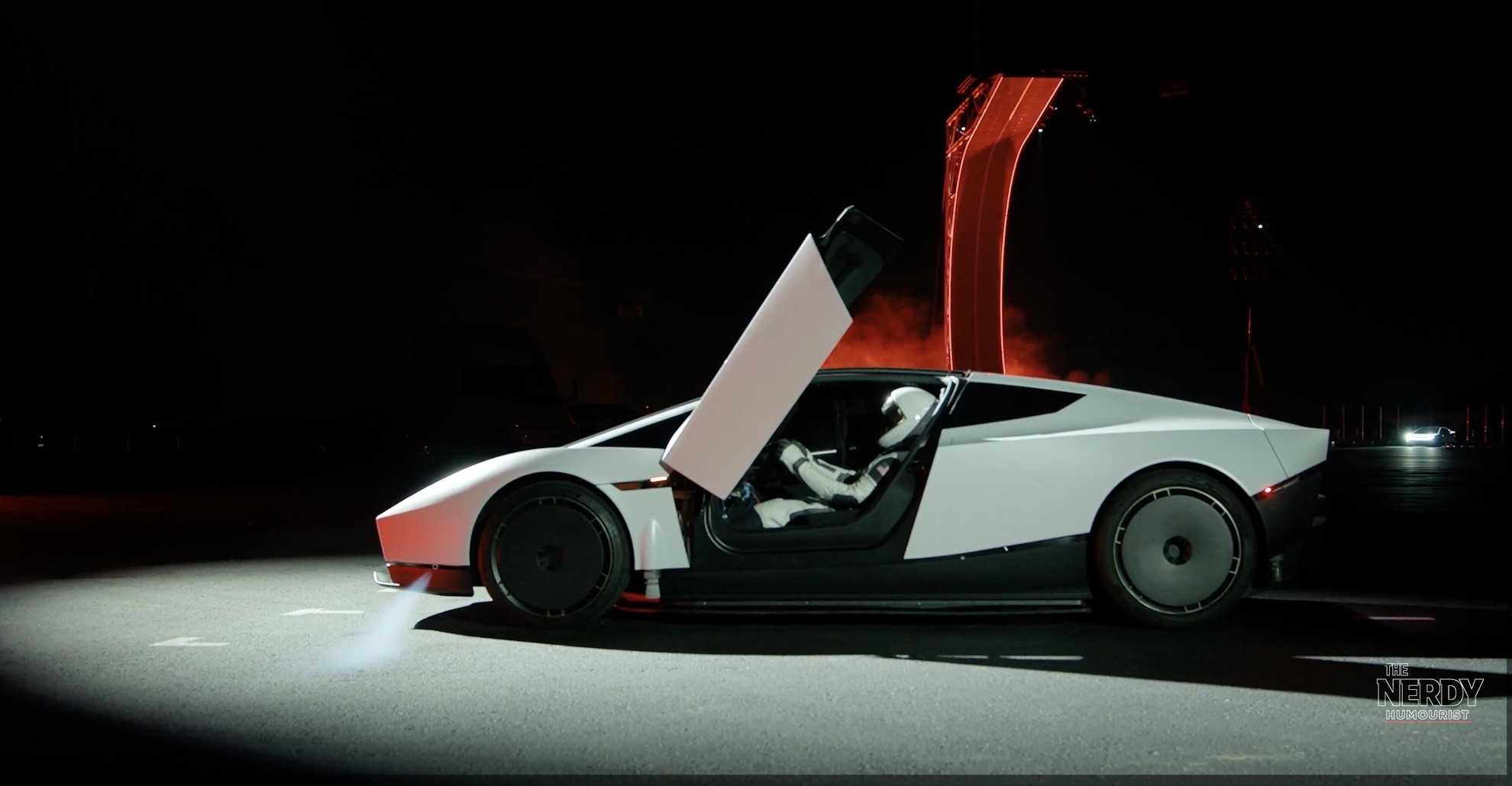 The Tesla Roadster with a spacesuit-clad driver inside and the red-lit halfpipe ramp behind it at the Tesla Roadster unveil event in McGregor, Texas