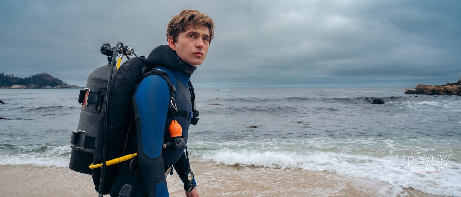 Austin Abrams as Jay Gardiner in a wetsuit with scuba gear, walking along the beach in the Whalefall movie