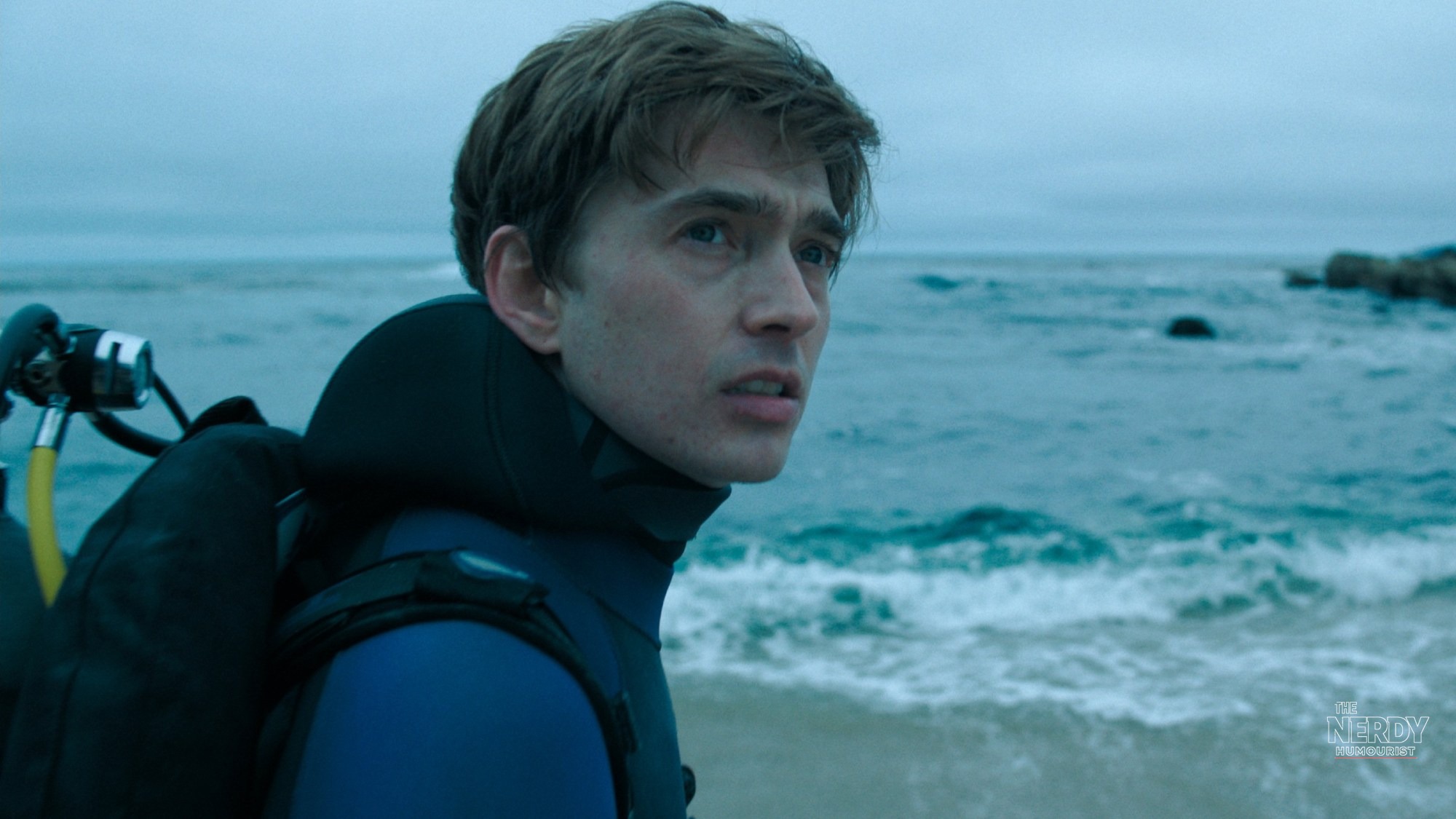 Close-up of Austin Abrams as Jay Gardiner in a wetsuit looking out at the ocean in the Whalefall movie